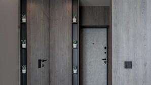 Un couloir moderne avec un lambris en bois, une porte dotée d’une poignée et des plantes en pot disposées sur des étagères.