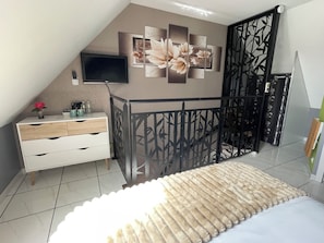 Un dormitorio con cama, cómoda, televisor montado en la pared y un panel decorativo.