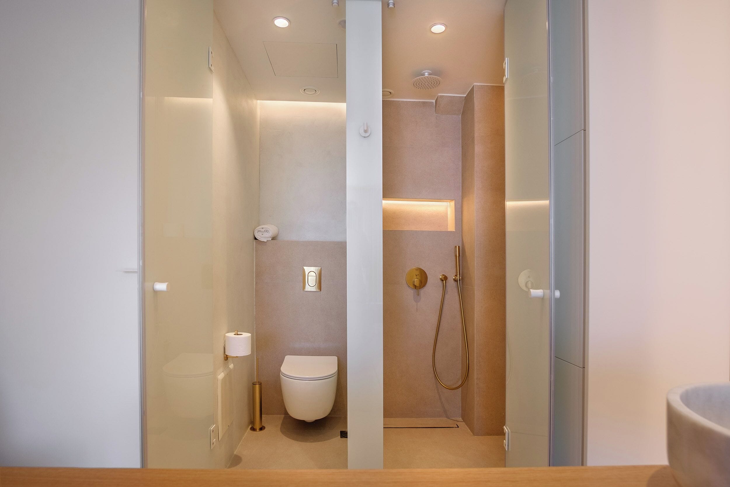 A modern bathroom with a glass partition, a toilet, a shower area, and a sink.