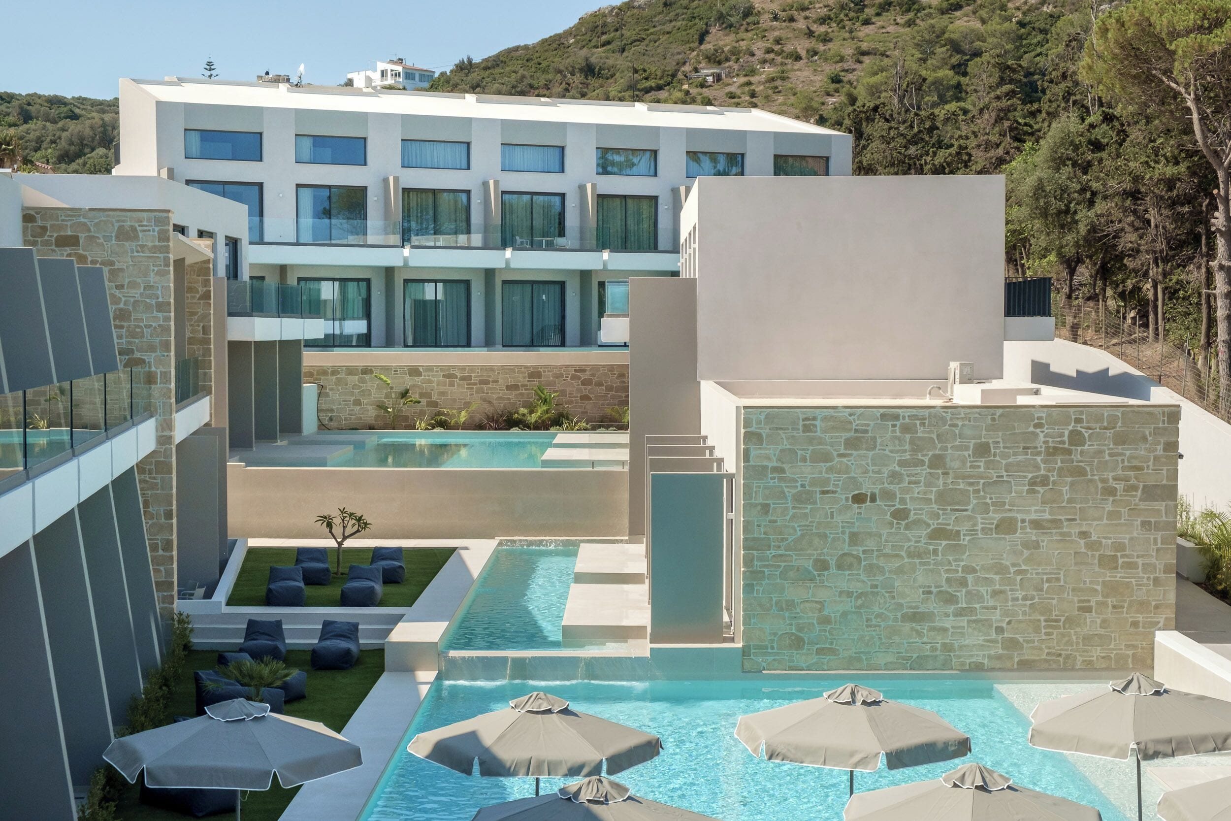 A modern hotel with a pool area, outdoor seating, and a view of the surrounding landscape.