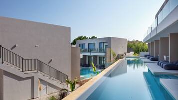 Zona de piscina moderna amb una piscina blava cristal·lina, una escala i un edifici amb grans finestres.