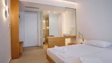 A modern hotel room with a large bed, a wooden nightstand, a mirror, and a bathroom visible through an open door.