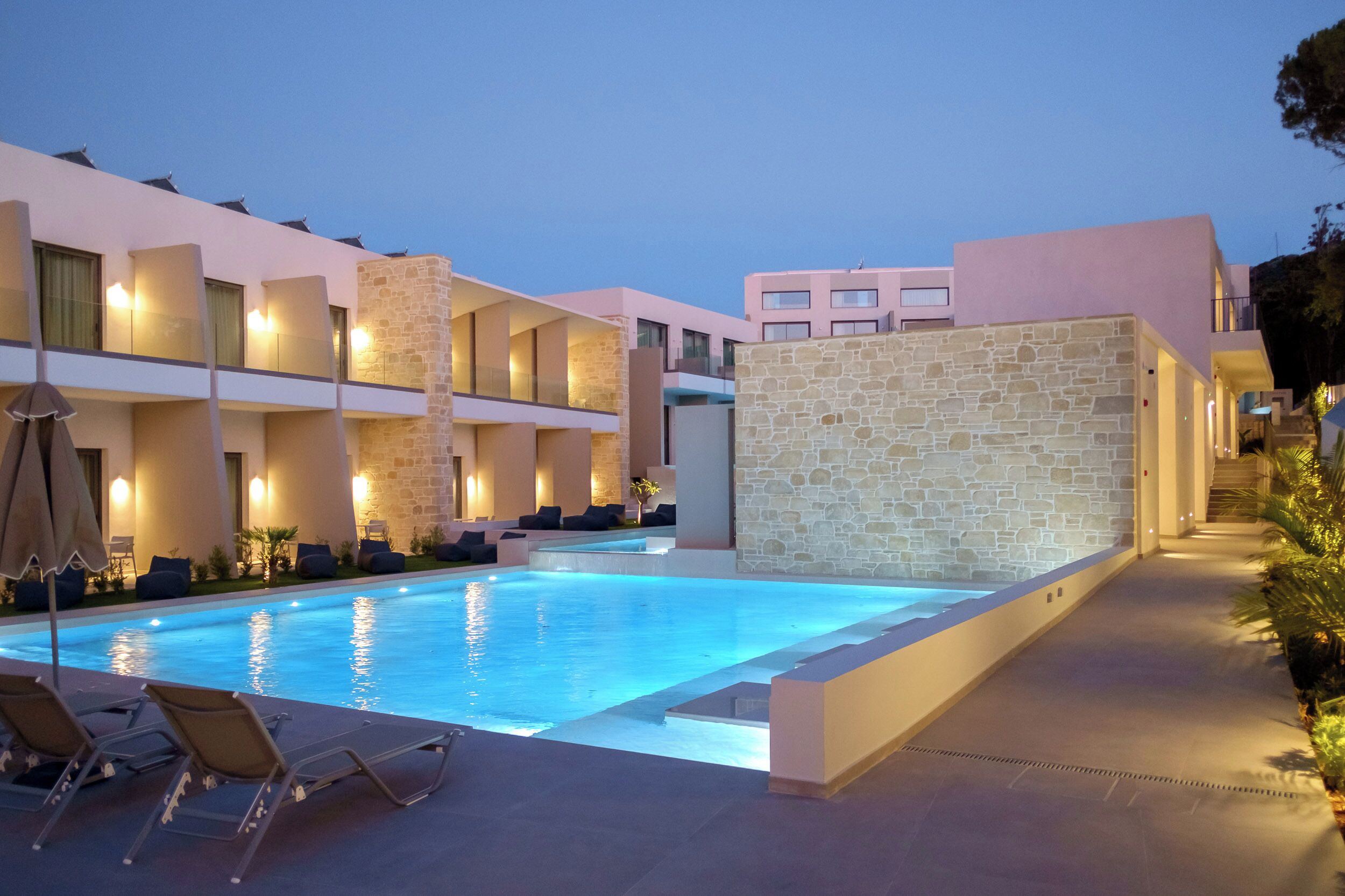 A modern hotel with a swimming pool, multiple balconies, and stone walls.