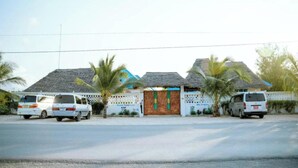 A row of white vans parked in front of a building with a thatched roof, surrounded by palm trees. - Serenity Boutique Hotel (Jambiani)