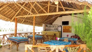 An outdoor seating area with thatched roof, wooden tables, and chairs. - Serenity Boutique Hotel (Jambiani)