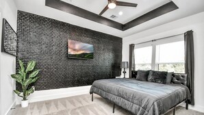 Un dormitorio moderno con una cama grande, una pared texturizada negra, un ventanal con cortinas y un ventilador de techo.
