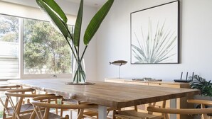 Ein Essbereich mit Holztisch und Stühlen, einer großen Pflanze in der Mitte und einem gerahmten Kunstwerk an der Wand.