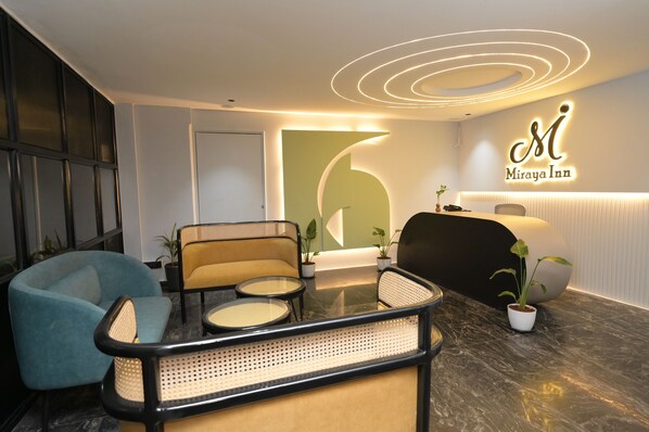 A modern reception area with a reception desk, seating area, and a large illuminated logo for Miraya Inn.