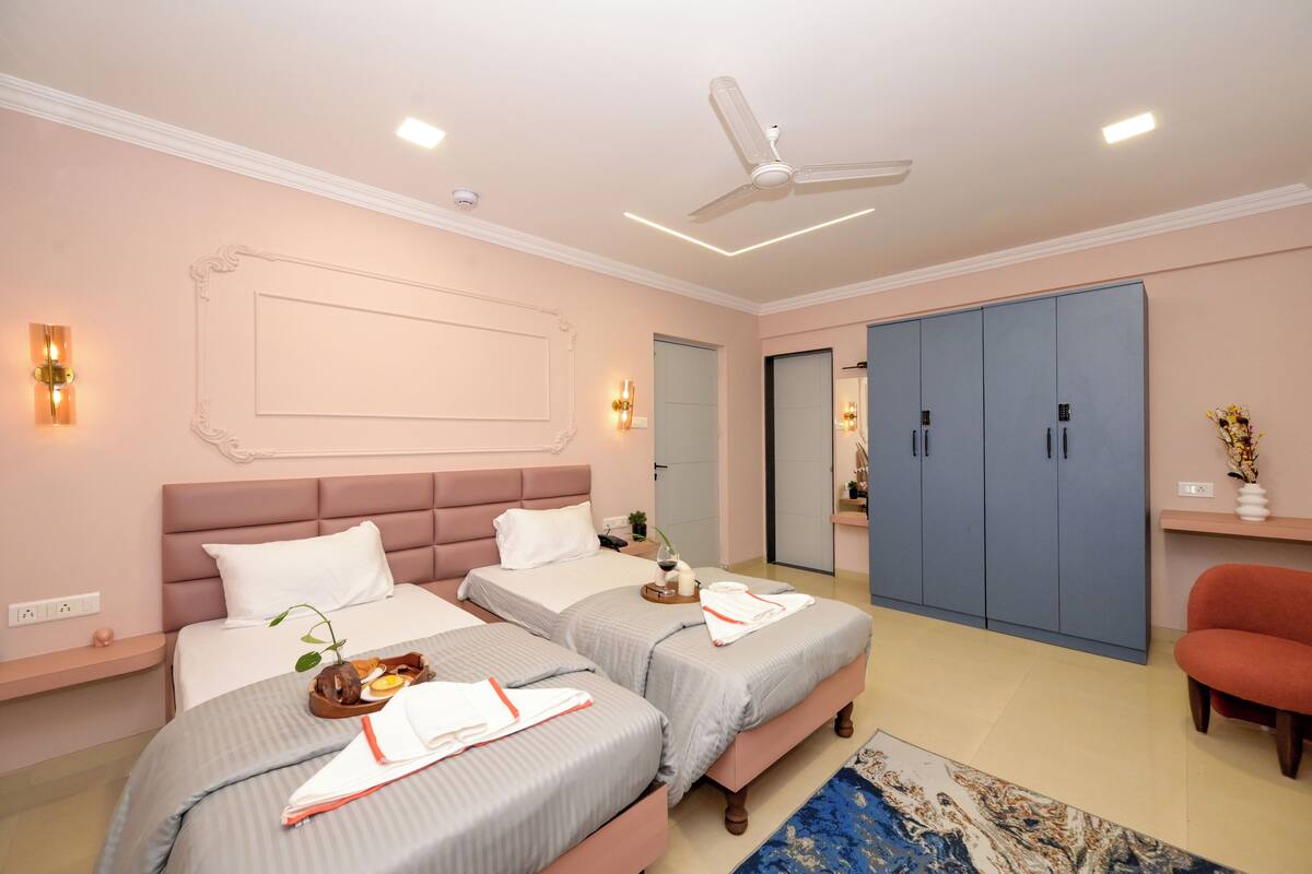 A hotel room with two beds, a ceiling fan, a wardrobe, and a small seating area.