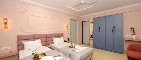 A hotel room with two beds, a ceiling fan, a wardrobe, and a small seating area.