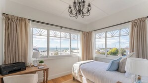 A bedroom with a bed, desk, chair, and large windows with a view. - Ocean Breeze - Modern Comfort with Outdoor Entertaining and Ocean Views (Parklands)