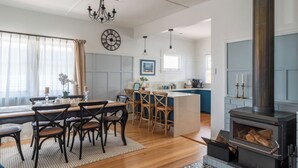 A modern kitchen with a central island, wooden chairs, a dining table, and a built-in wood-burning stove. - Ocean Breeze - Modern Comfort with Outdoor Entertaining and Ocean Views (Parklands)