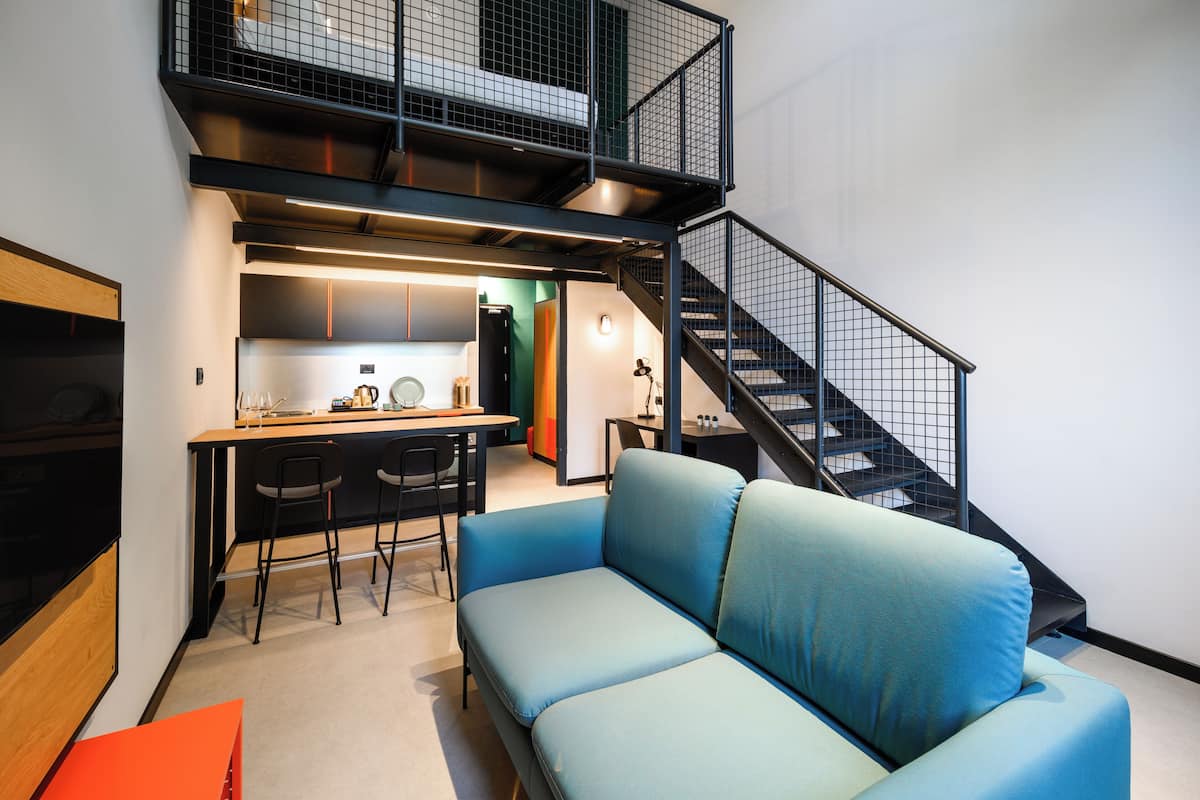 A modern apartment with a kitchenette, a blue sofa, and a staircase.
