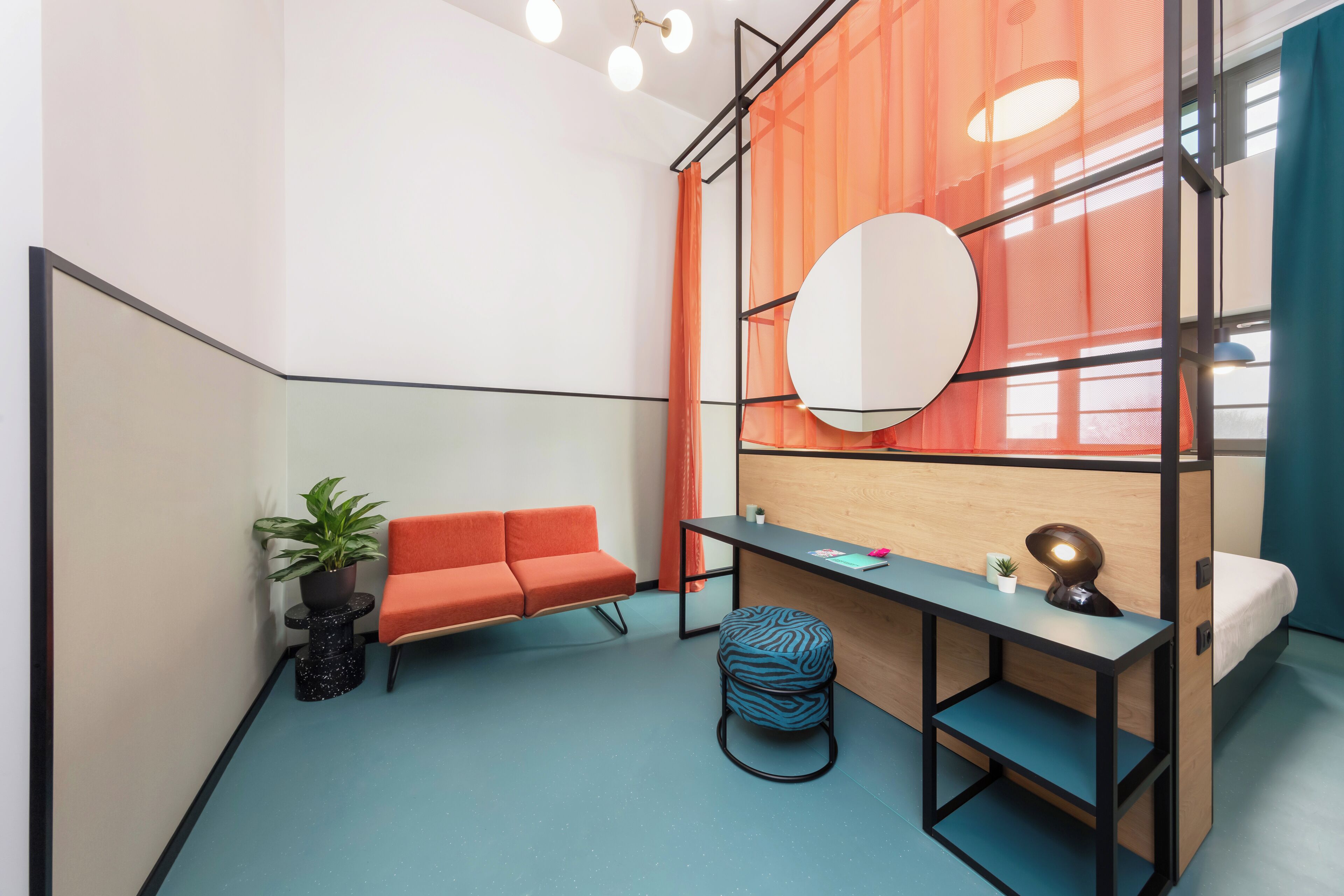 Ein gemütlicher Raum mit Schreibtisch, orangefarbenem Sofa und einem kleinen Blumentopf.