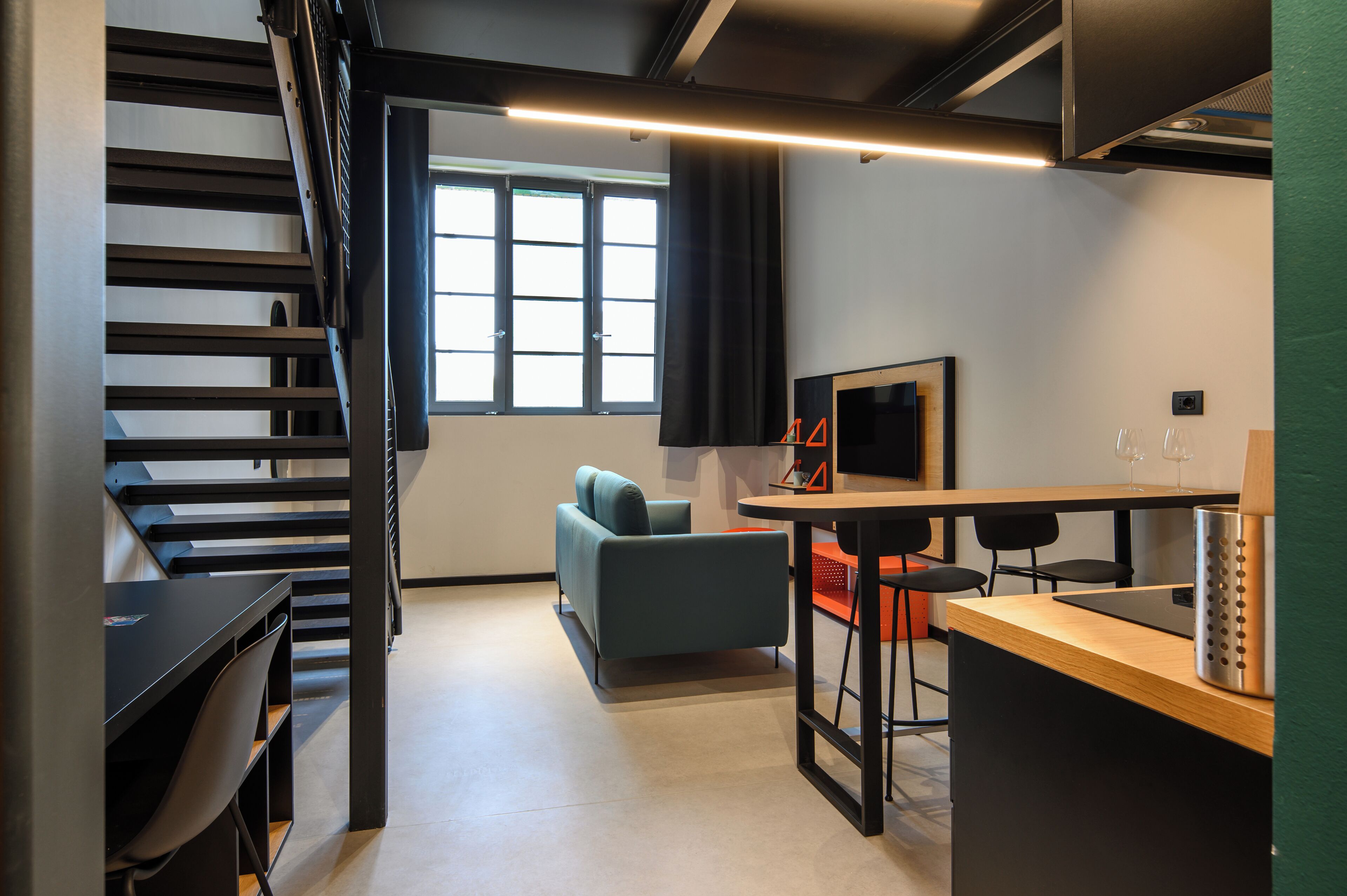 A modern interior with a staircase, a sofa, a dining area, and a TV.