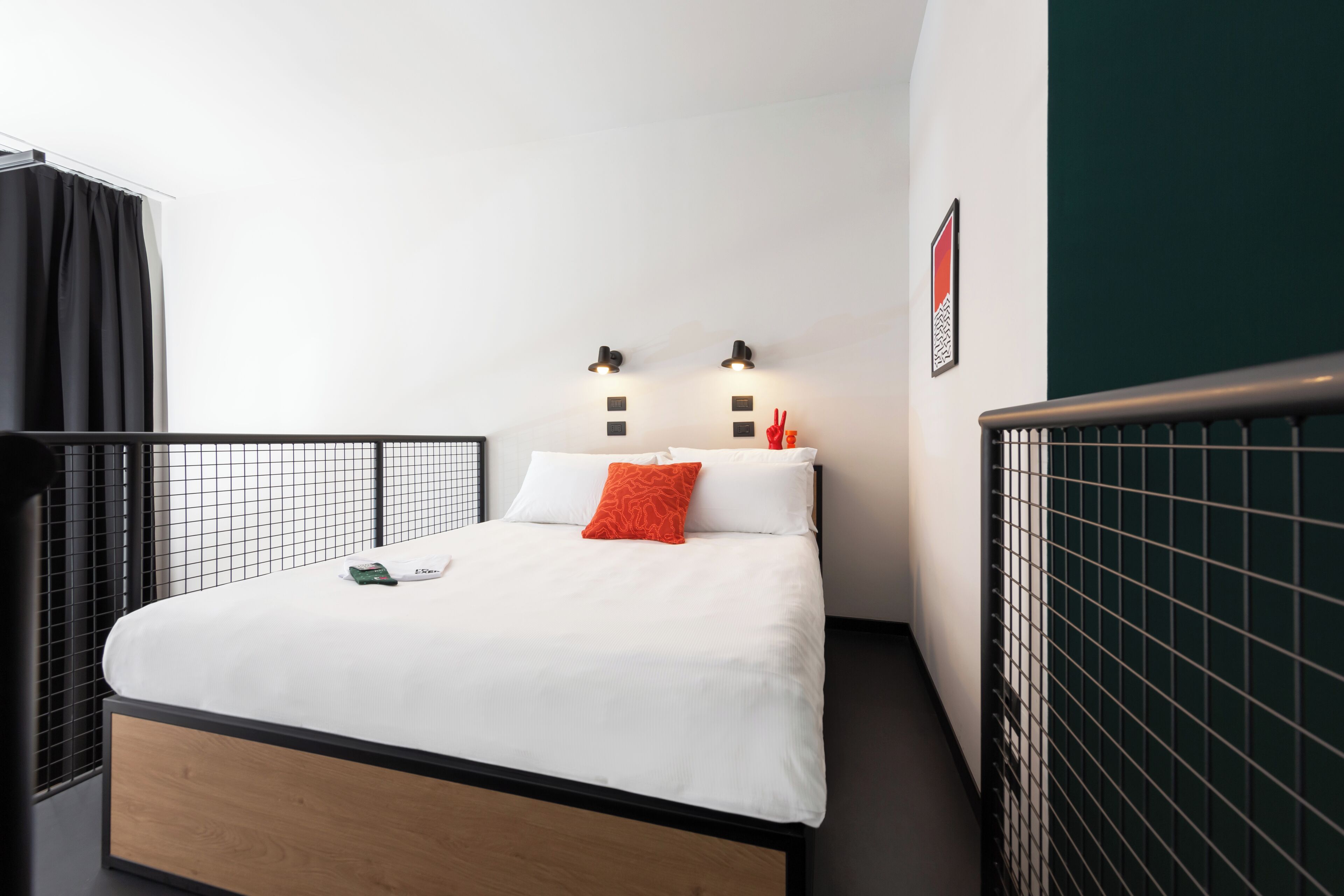 Quarto de hotel moderno com uma cama de solteiro, uma mesinha de cabeceira e vista para a cidade.