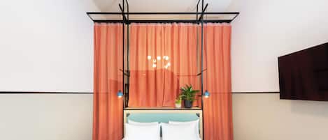 Una habitación de hotel moderna con una cama, cortinas naranjas, una planta en maceta y un televisor montado.