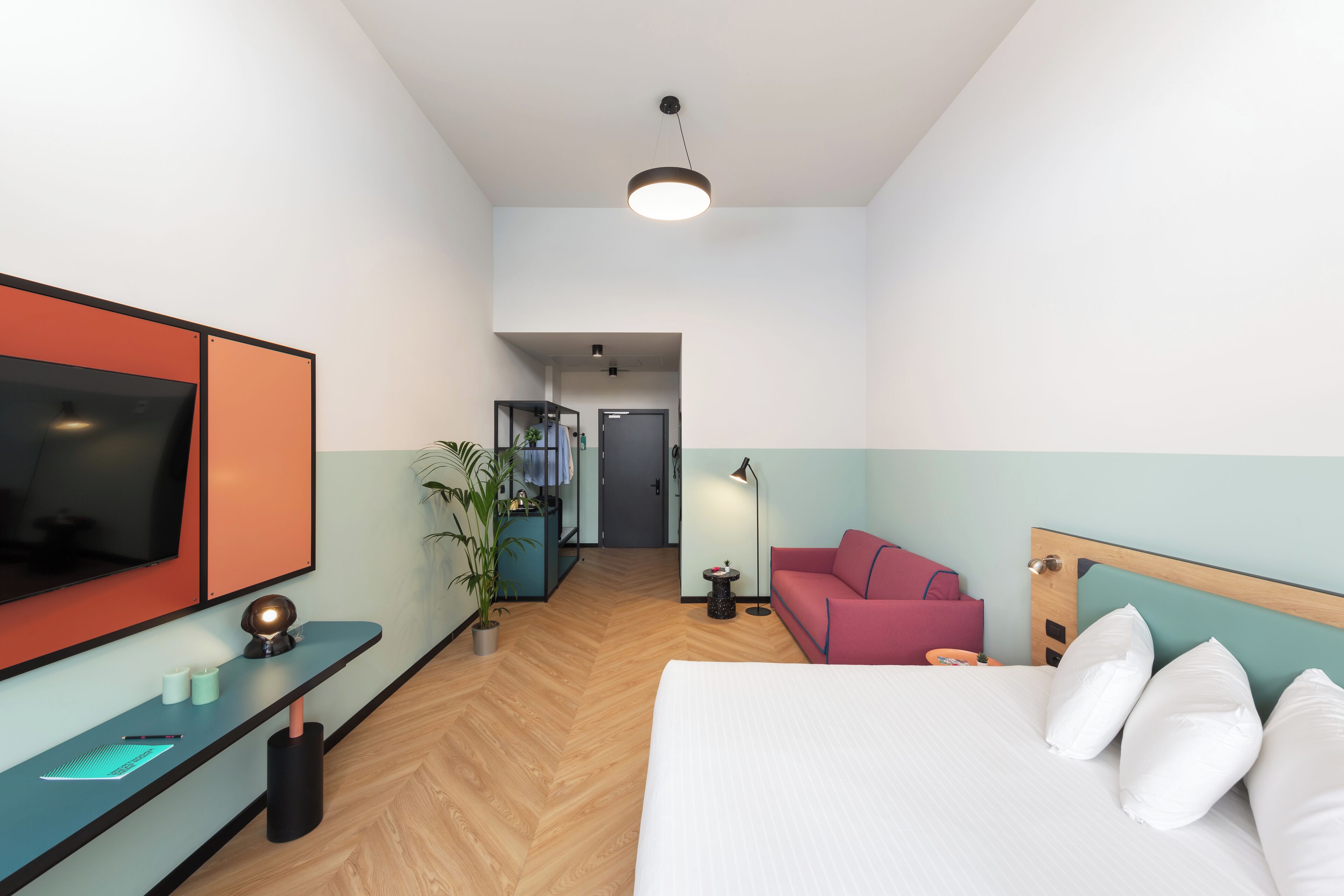 Una habitación de hotel con una cama, un escritorio con televisor, un sofá rojo y una planta en maceta.