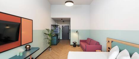Et hotelværelse med seng, skrivebord med TV, rød sofa og en potteplante.