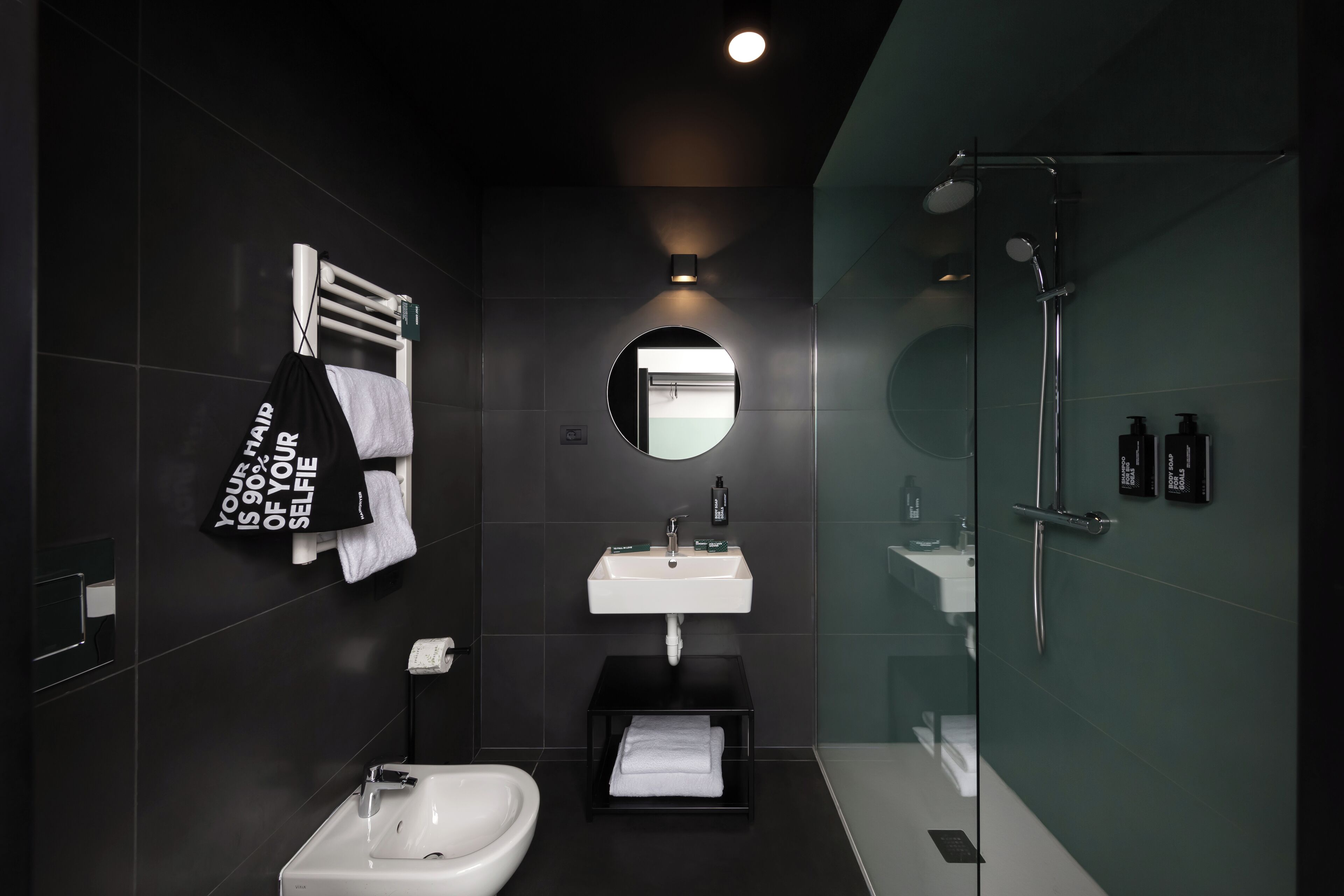 Un baño moderno con un lavamanos blanco, un espejo, una ducha con cerramiento de vidrio y un toallero negro con una toalla.