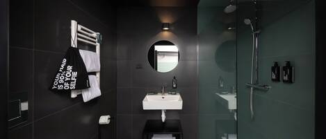 A modern bathroom with a white sink, a mirror, a glass-enclosed shower, and a black towel rack with a towel.