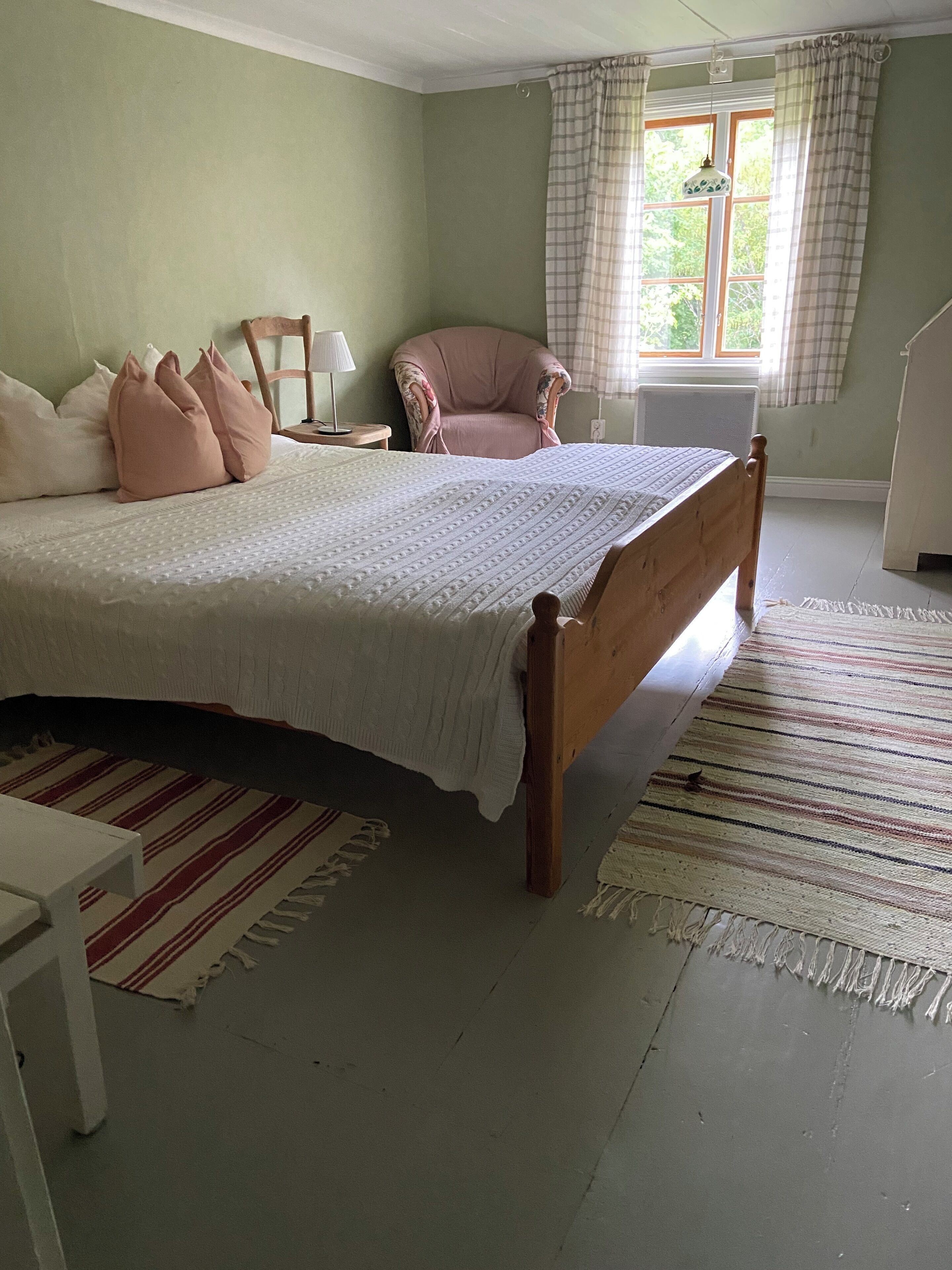 Une chambre à coucher avec un grand lit, une chaise, une lampe et une fenêtre avec des rideaux.