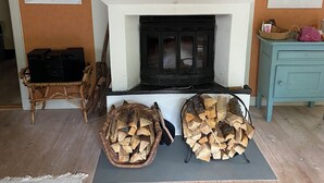 Una sala de estar con chimenea, dos cestas de leña, un armario azul y dos cuadros en las paredes.