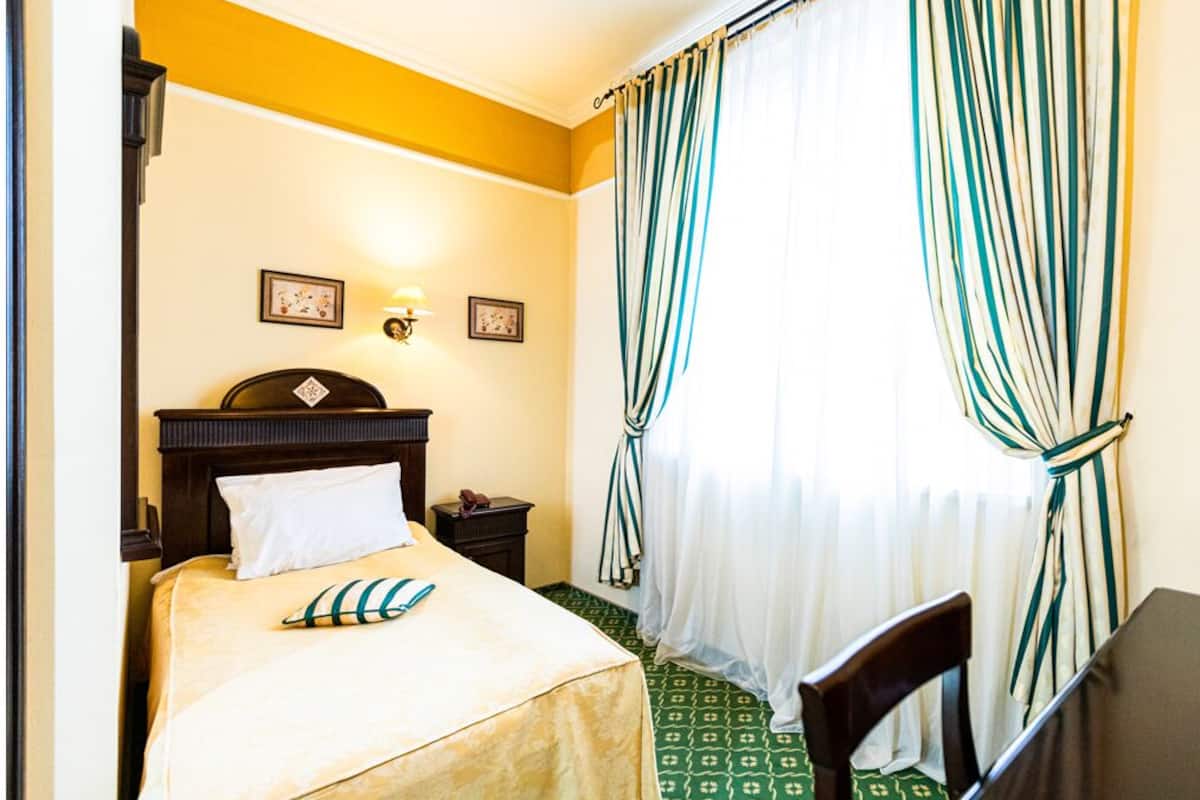 A hotel room with a bed, a nightstand, a chair, and a window with curtains.