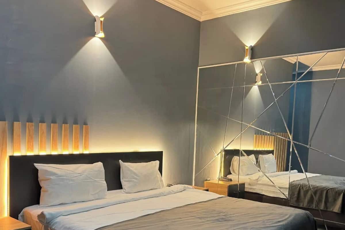 Une chambre à coucher moderne avec un grand lit, des tables de chevet, un miroir fixé au mur et un éclairage d’ambiance.