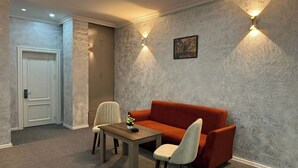 Ein Zimmer mit einer roten Couch, einem Holztisch und zwei Stühlen. Eine Tür und eine Wandleuchte sind ebenfalls vorhanden.