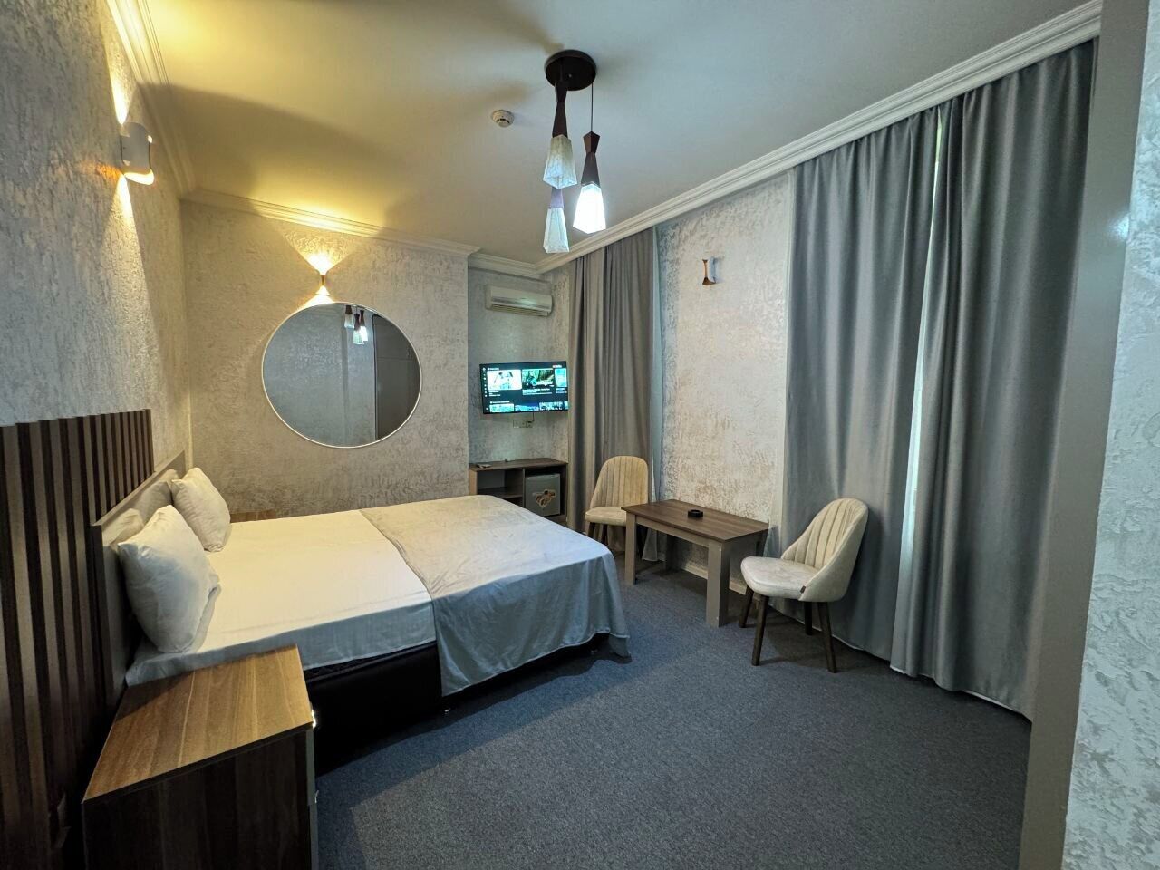 Ein Hotelzimmer mit Bett, Schreibtisch, Stuhl, Fernseher und einem großen Fenster mit Vorhängen.