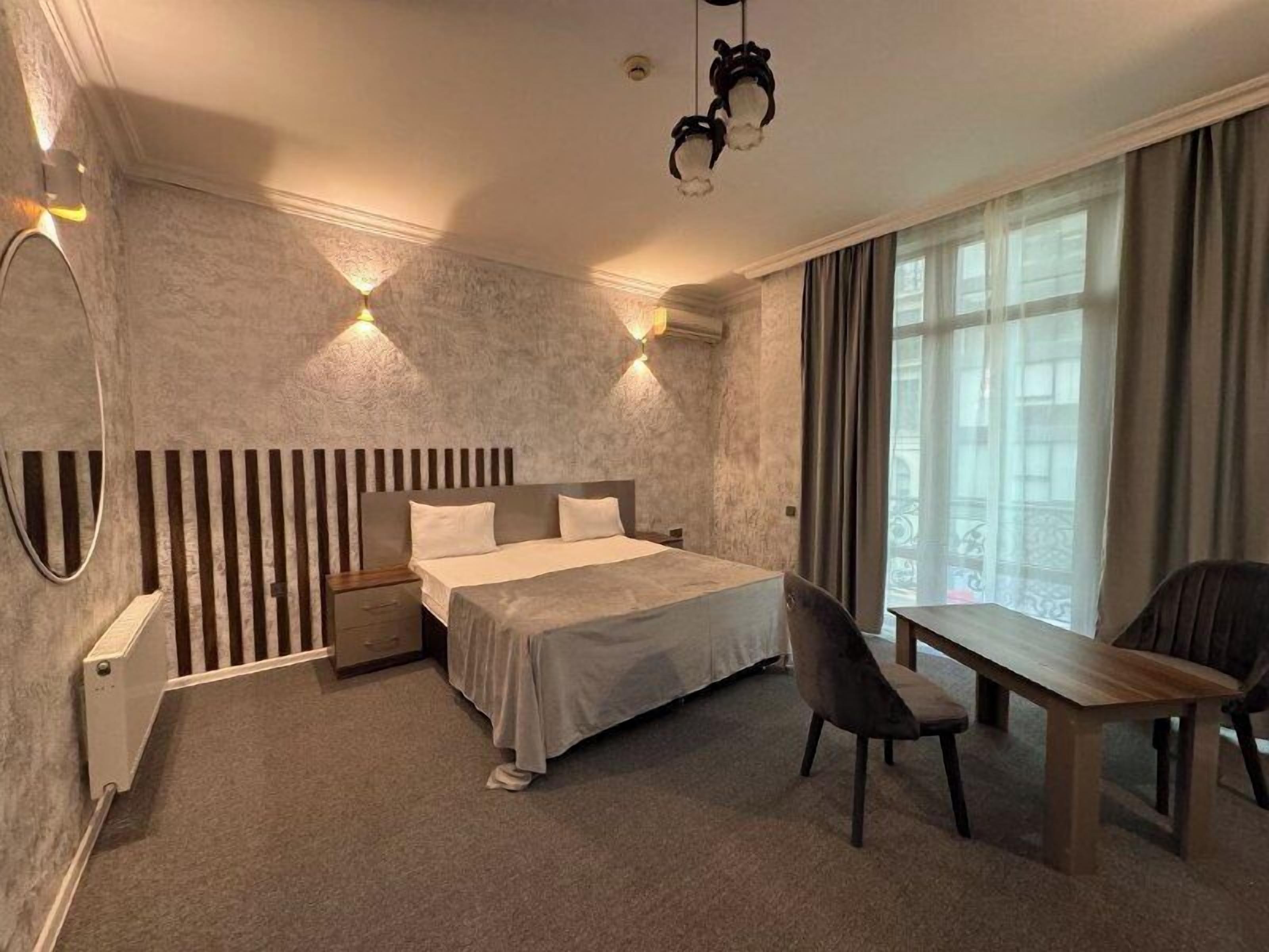 A modern hotel room with a bed, a desk, a chair, and a large window.