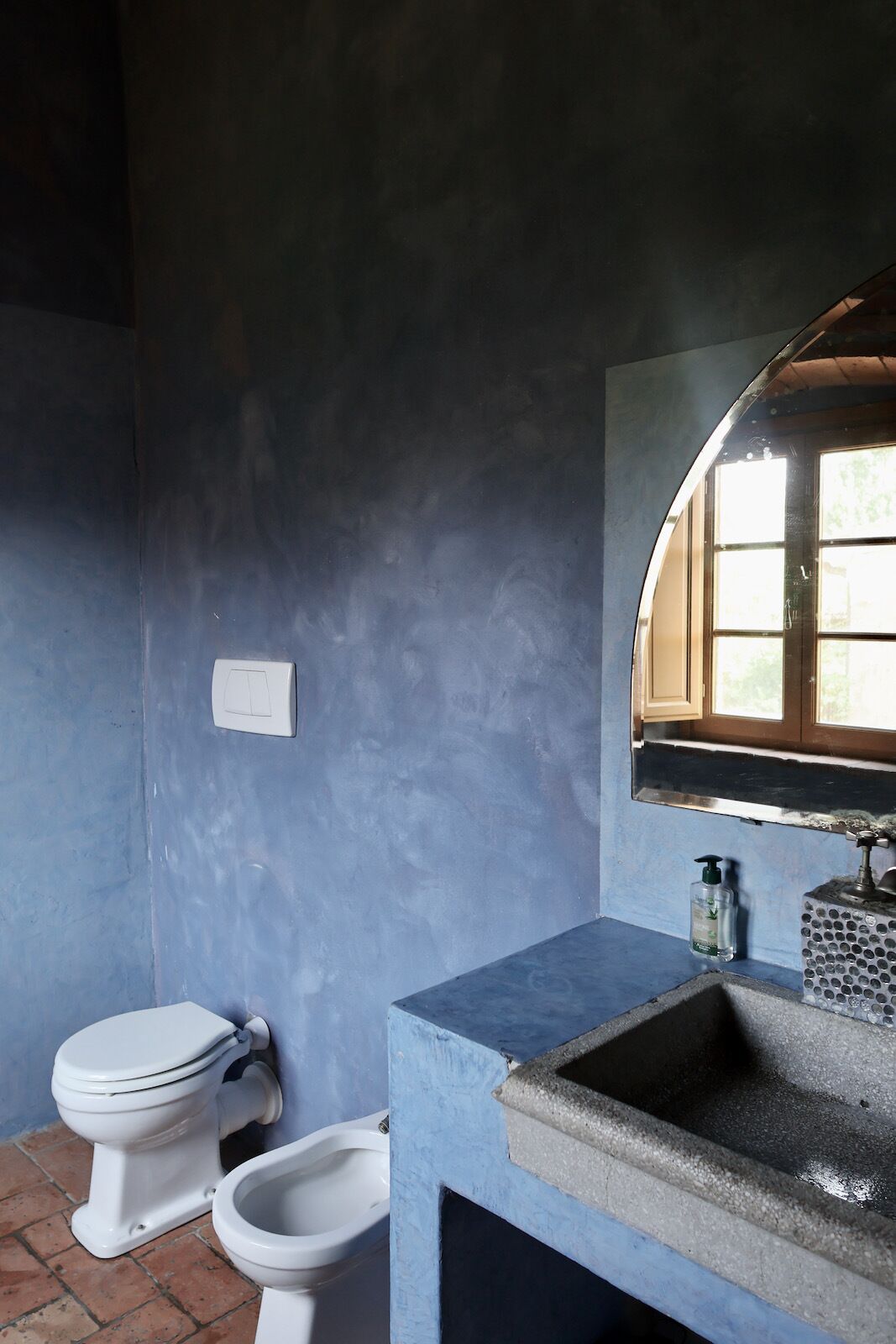 Une salle de bain avec un mur bleu, une fenêtre, un lavabo et deux toilettes.