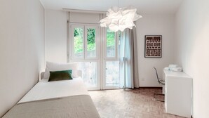 A bedroom with a bed, a desk, and a window with a view of greenery. - App. near italian border (Pink Flat 2) (Chiasso)