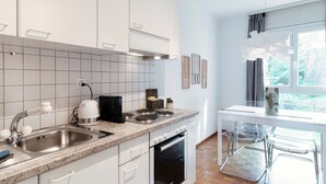 A modern kitchen with white cabinets, a stainless steel sink, and a built-in oven. There is a window with a view of greenery outside. - App. near italian border (Pink Flat 2) (Chiasso)