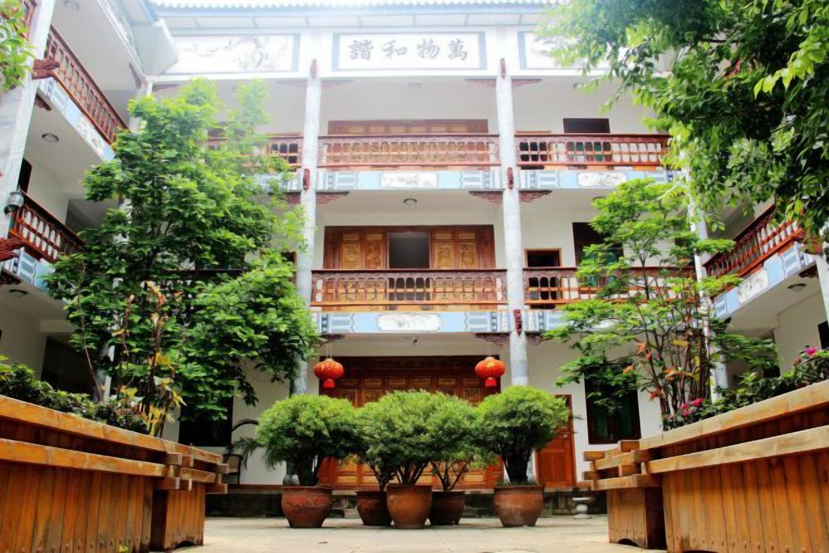 A traditional courtyard with multiple levels of balconies, potted plants, and a central wooden structure.