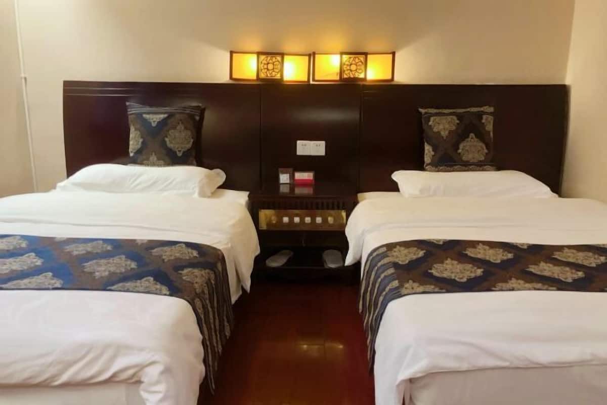 A hotel room with two beds, a nightstand, and a wall-mounted lamp.