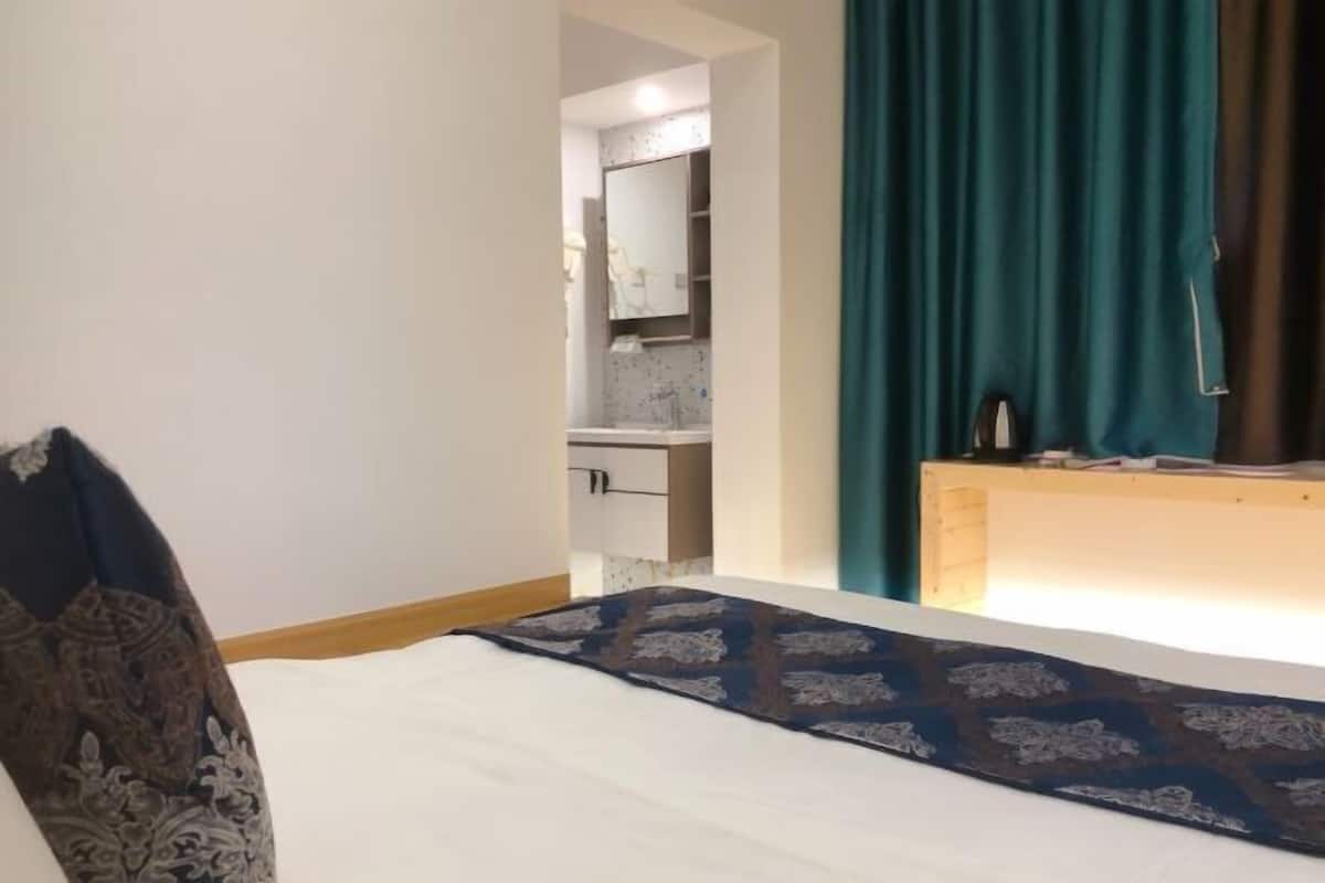 A bedroom with a bed, a wooden nightstand, a mirror, and a view of a bathroom.