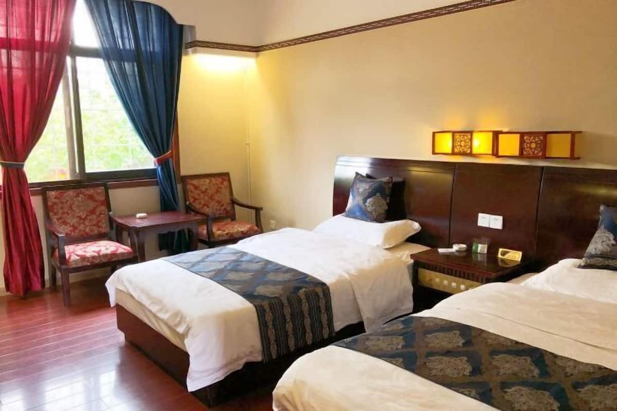 A hotel room with two beds, a chair, a bedside table, and a window with curtains.