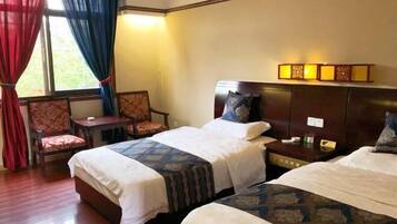 A hotel room with two beds, a chair, a nightstand, and a window with curtains.