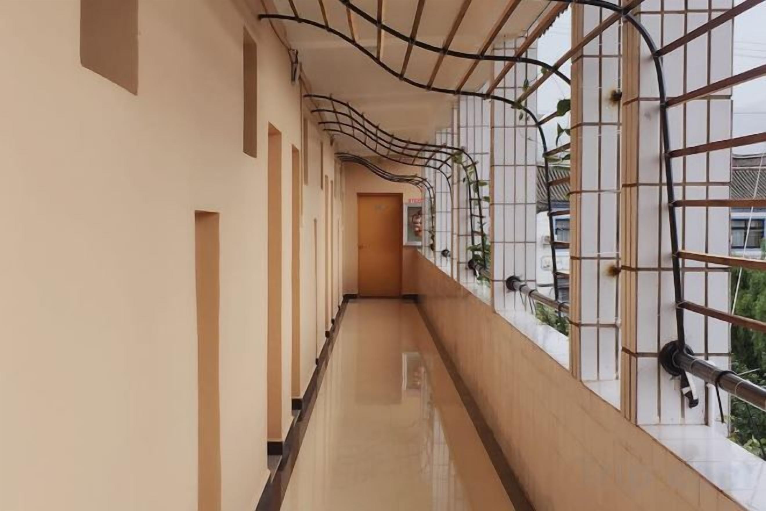 Un pasillo con piso reflectante, varias puertas y vista al exterior a través de una ventana con celosía metálica.