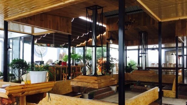 A spacious indoor area with wooden benches and tables, large windows, and potted plants. - New Hotel Busan (Weishan)
