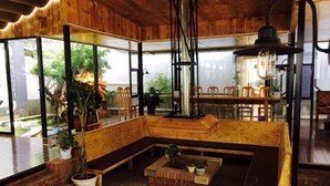 A wooden interior with a large bench, potted plants, and a dining area with chairs. - New Hotel Busan (Weishan)
