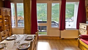 Ett mysigt rum med ett träbord dukat för middag, stora fönster med röda gardiner och utsikt över en grönskande sluttning.