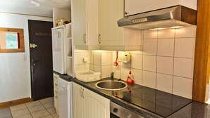 Ett kompakt kök med vita skåp, en diskho i rostfritt stål, en inbyggd ugn och en svart bänkskiva.