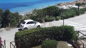 A coastal view with a white car parked near a pedestrian crossing, overlooking a beach with people and umbrellas. - Beachfront house with breathtaking views  (Pula)