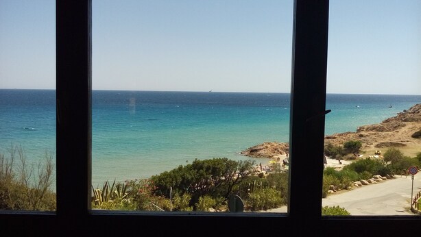A coastal view through a window, featuring a clear sea, rocky terrain, and sparse vegetation. - Beachfront house with breathtaking views  (Pula)