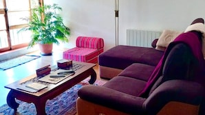 En stue med en sofa, et sofabord, en stribet skammel, en potteplante og en gulvlampe.