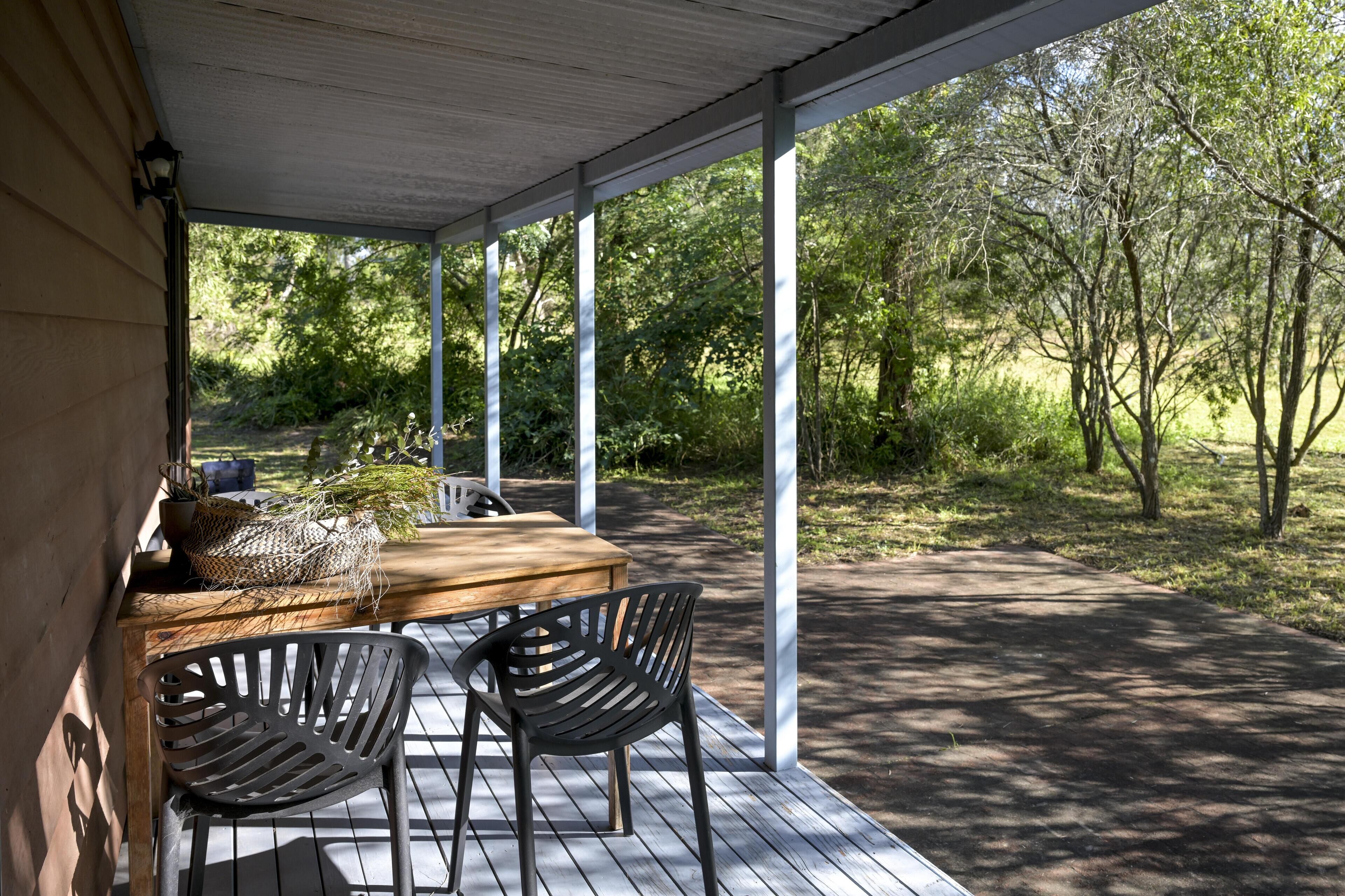 Pátio externo com mesa de madeira e duas cadeiras, cercado por uma área coberta com pilares brancos.