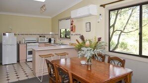 Una cocina con comedor, refrigerador, estufa, microondas y ventana con vista a árboles.